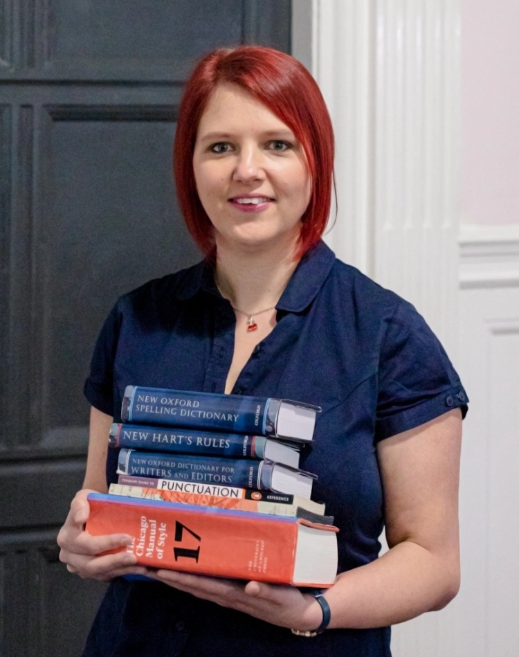 Claire Cronshaw Cherry Edits holding a stack of books in front of a door that says Reading Room