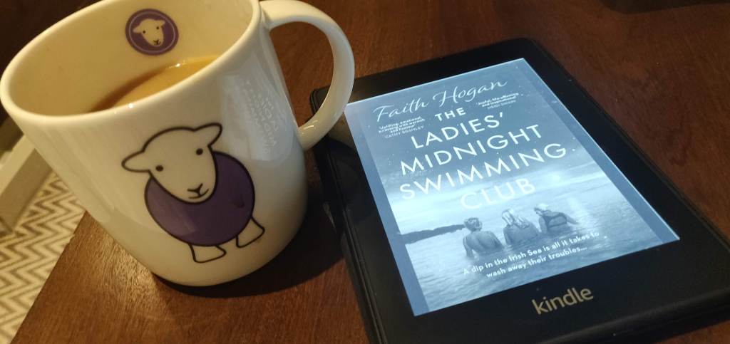 Mug of tea and a Kindle showing Faith Hogan's The Ladies' Midnight Swimming Club